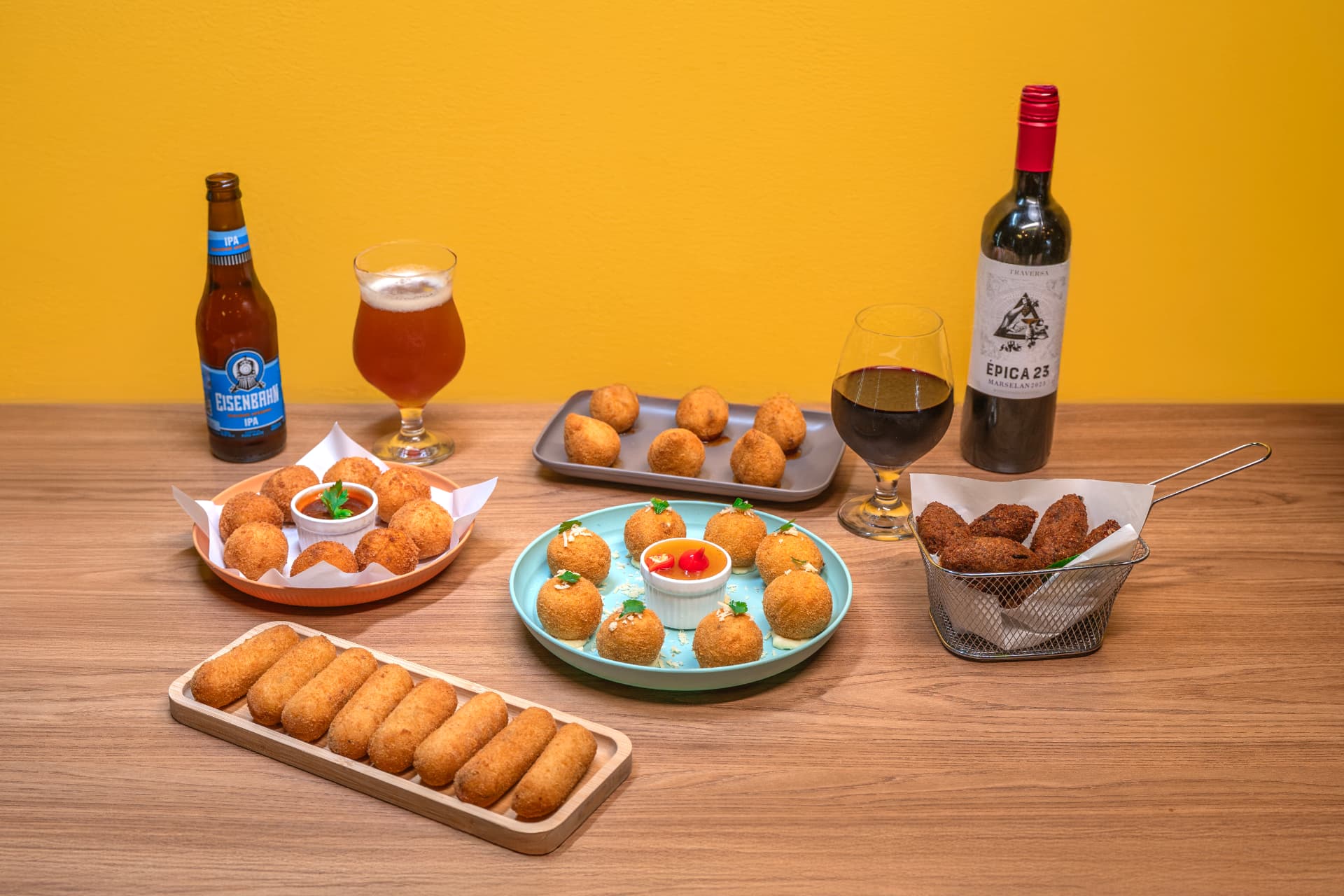 Mesa farta com croquetes, bolinhos e salgados acompanhados de cerveja e vinho tinto