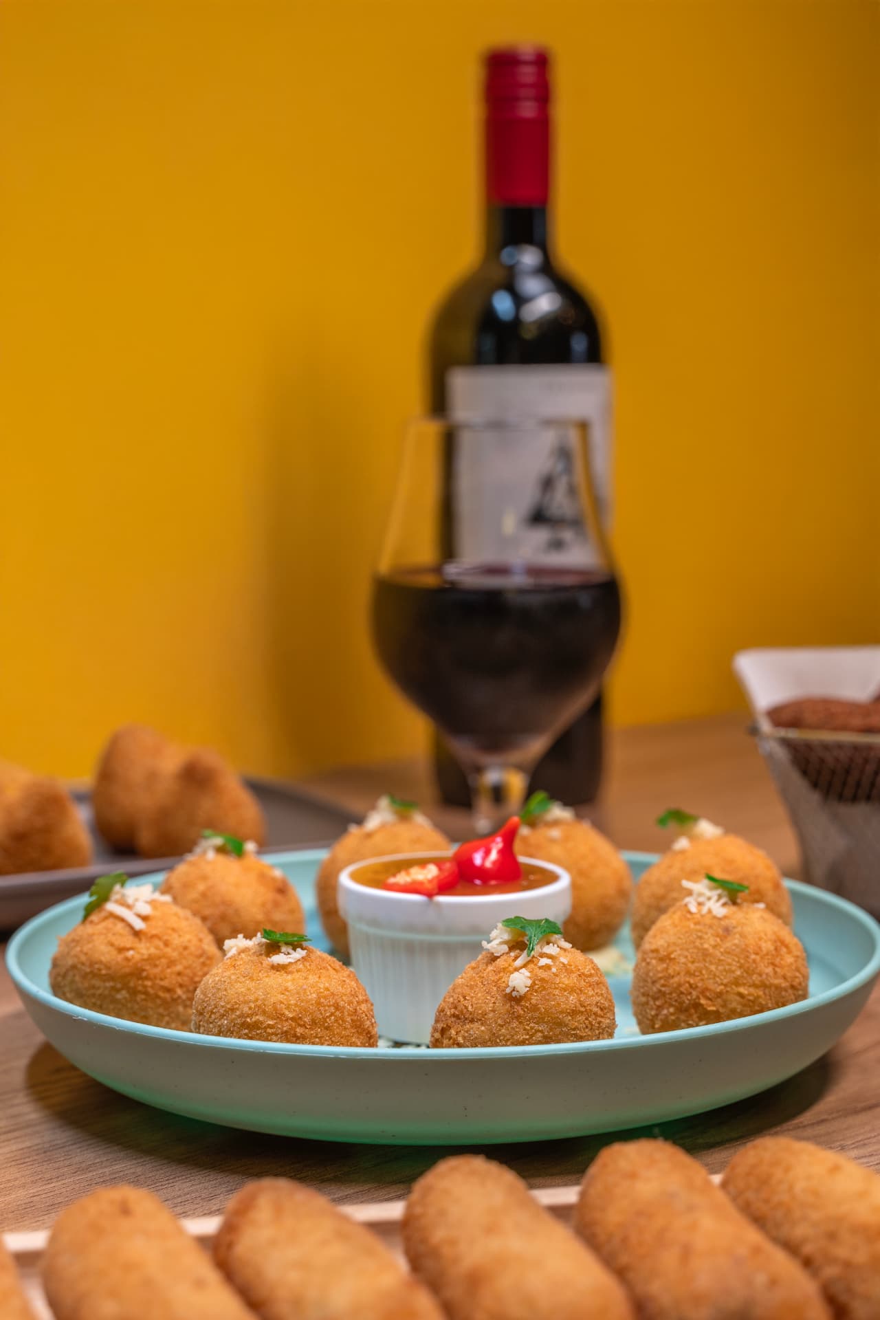 Bolinhos dourados servidos em prato azul com molho e taça de vinho